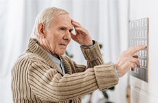 [Translate to Japanese:] Old man touching his forehead standing infront of an button panel
